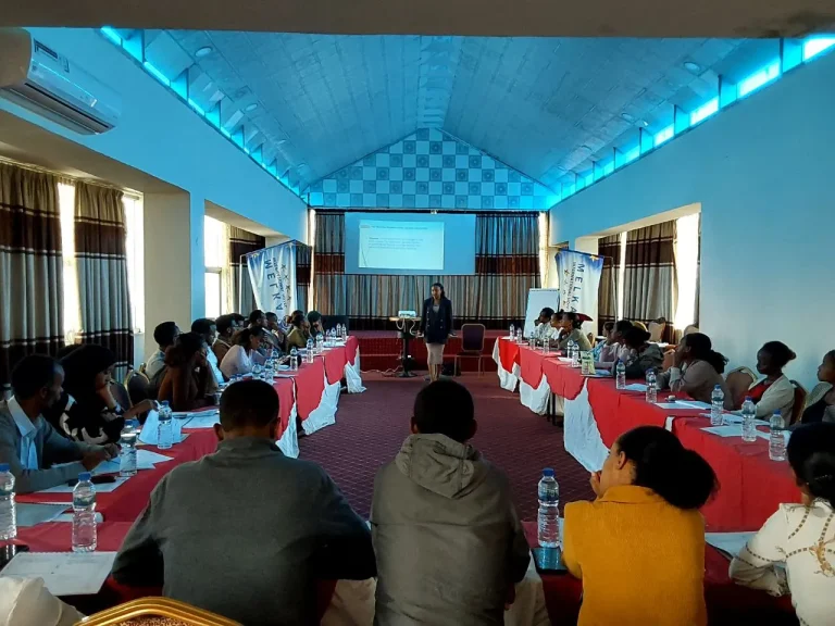 Participants seated around U-shaped tables in a training hall.